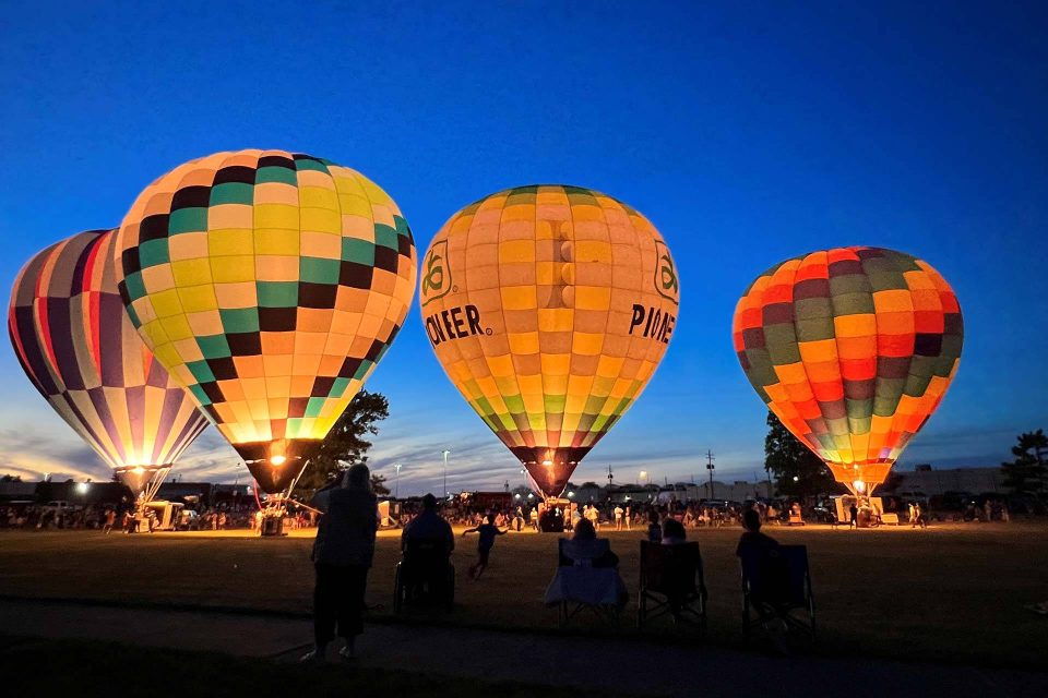Four hot air balloons on the ground at night with bright blue skies.