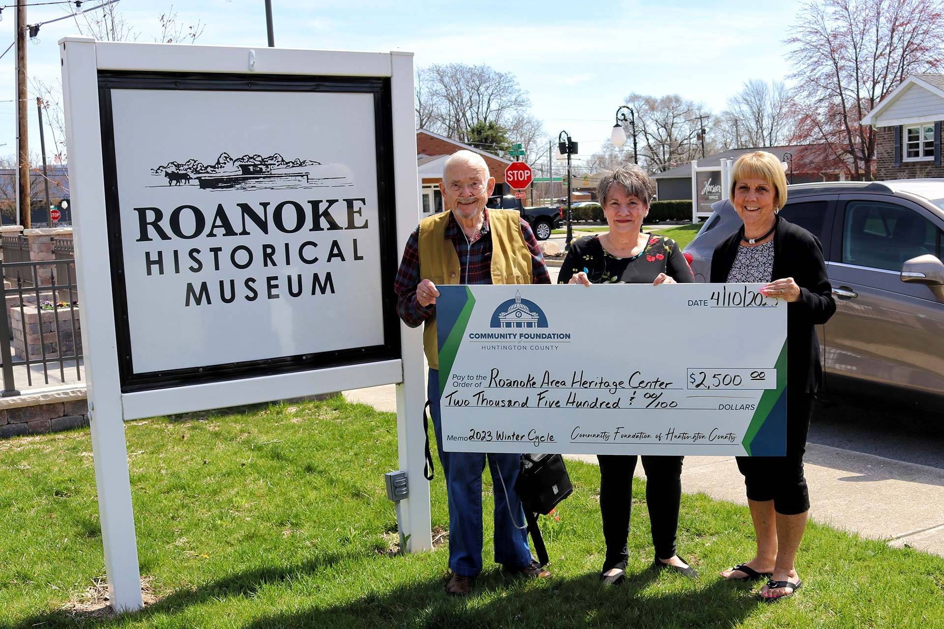Three adults holding a check for the Roanoke Area Heritage Center for $2,500 in front of the Roanoke Historical Museum sign.