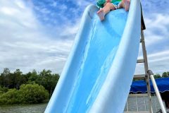 Boy sitting at the top of a waterslide wearing a puddlejumper floatie.