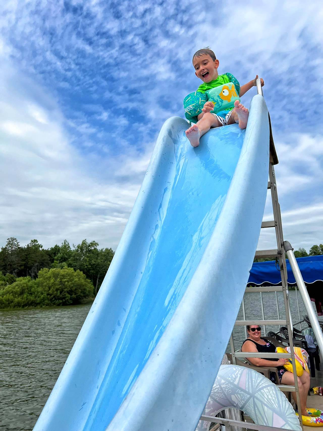 Boy sitting at the top of a waterslide wearing a puddlejumper floatie.