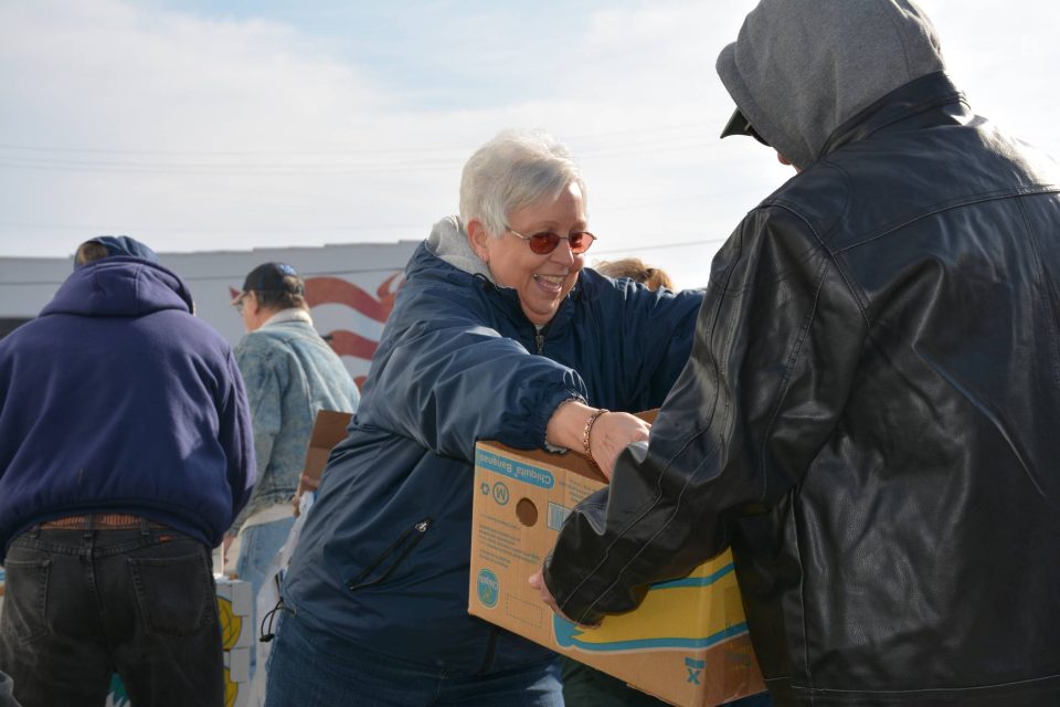 Older woman volunteering and taking boxes during community harvest event.