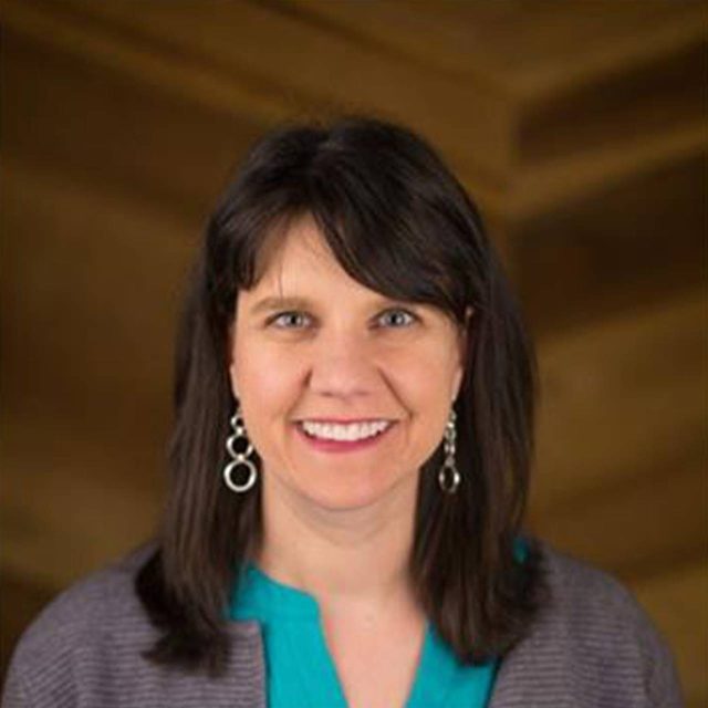 Head shot of Janet wearing a gray sweater over a teal blouse with silver earrings